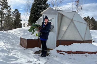 Woman holding a large basket of produce standing outside a greenhouse with snow on the ground