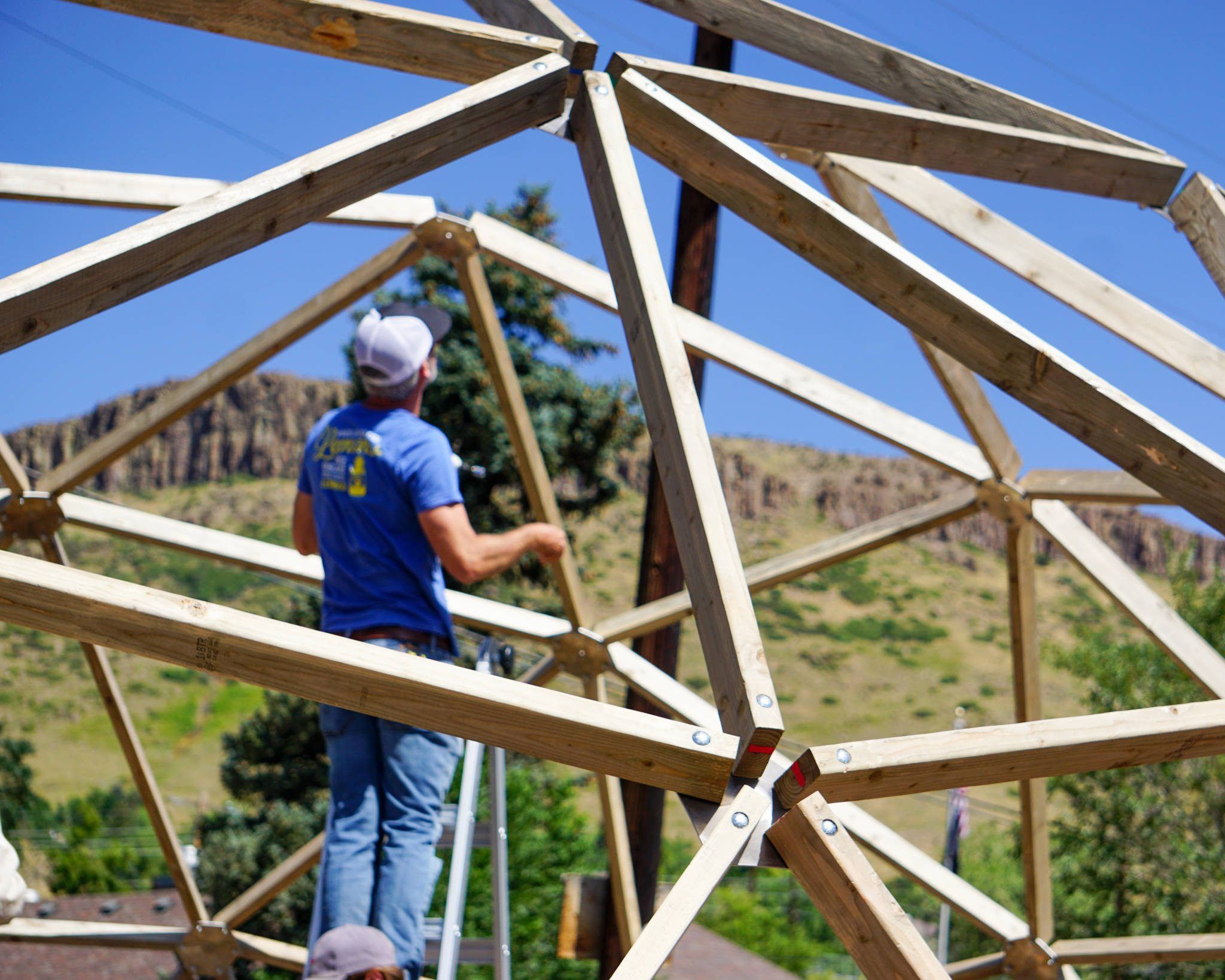 geodesic dome greenhouse under construction the struts and hub are in focus in the foreground while a person on a ladder is blurred in the background