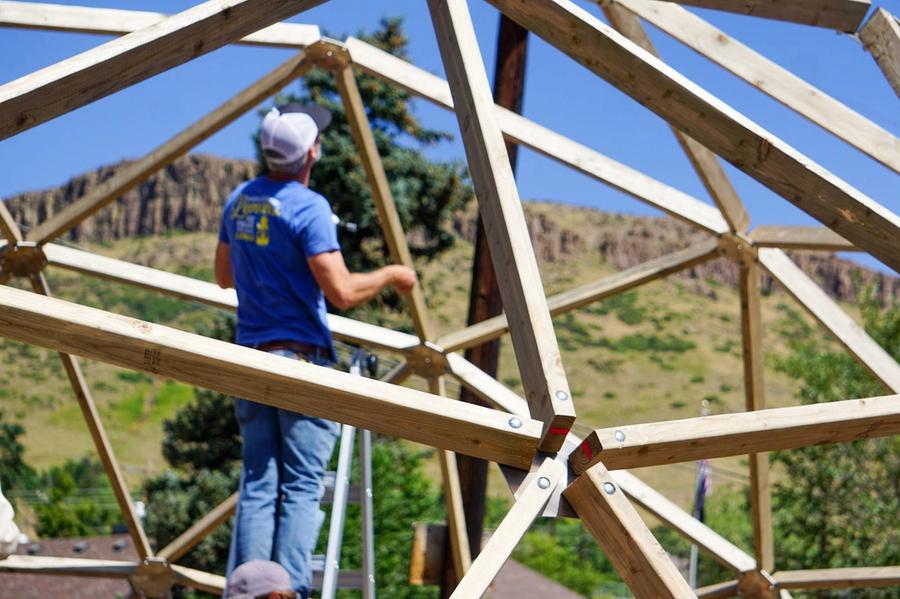 geodesic dome greenhouse under construction the struts and hub are in focus in the foreground while a person on a ladder is blurred in the background