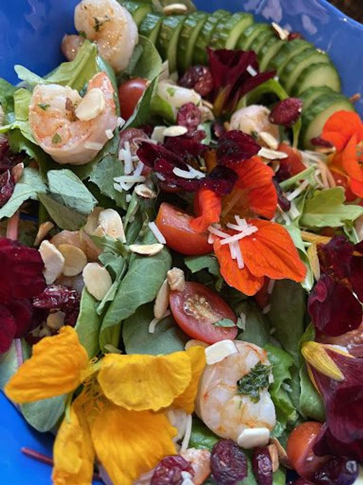 colorful salad featuring shrimp and nasturtiums on a blue plate
