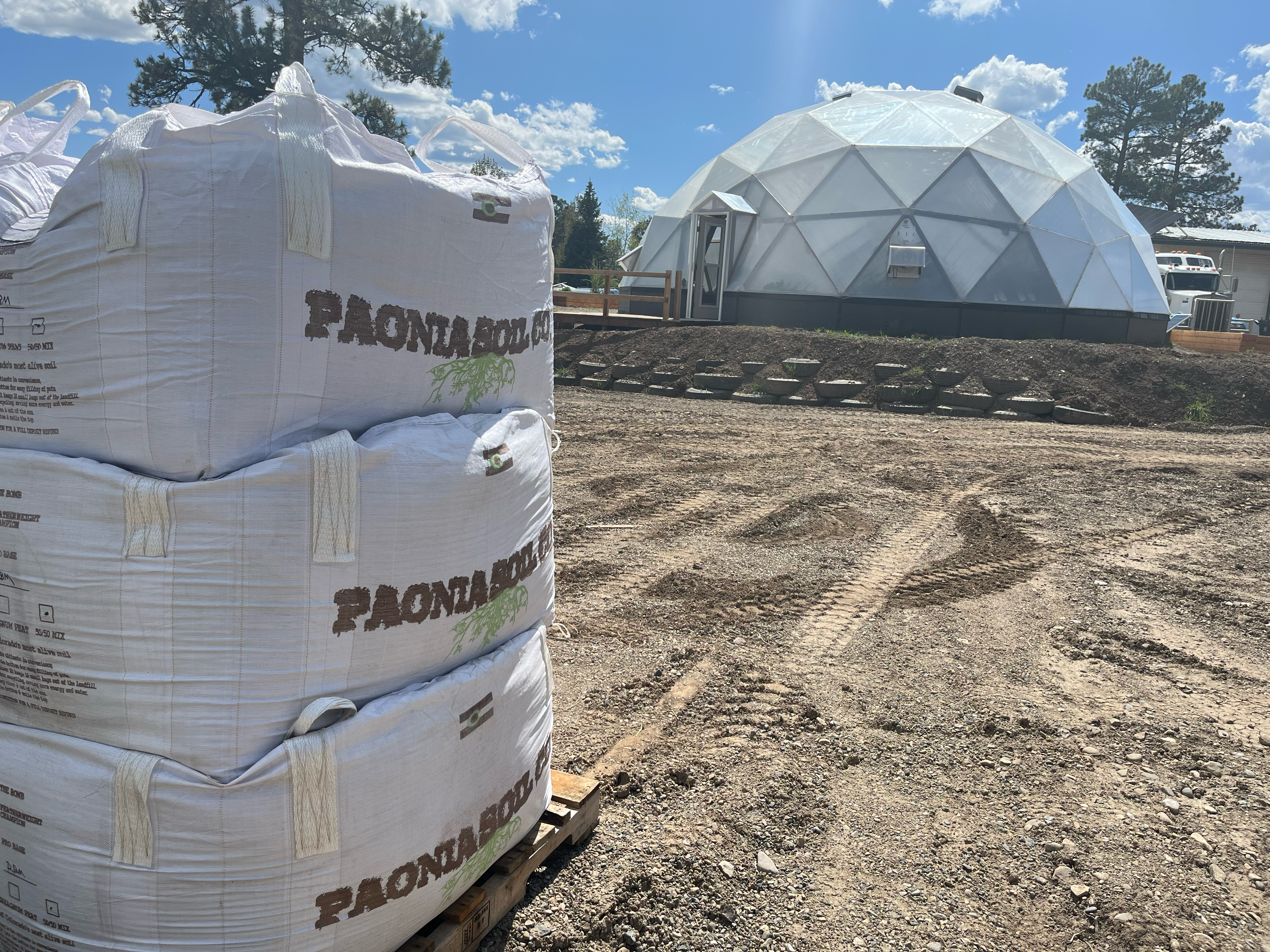 Three one cubic yard totes of paonia soil stacked on a pallet with a growing dome in the background