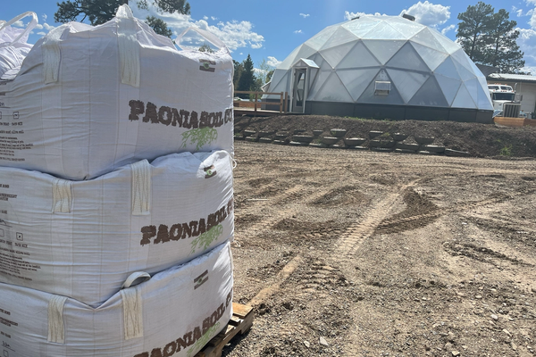 Three one cubic yard totes of paonia soil stacked on a pallet with a growing dome in the background