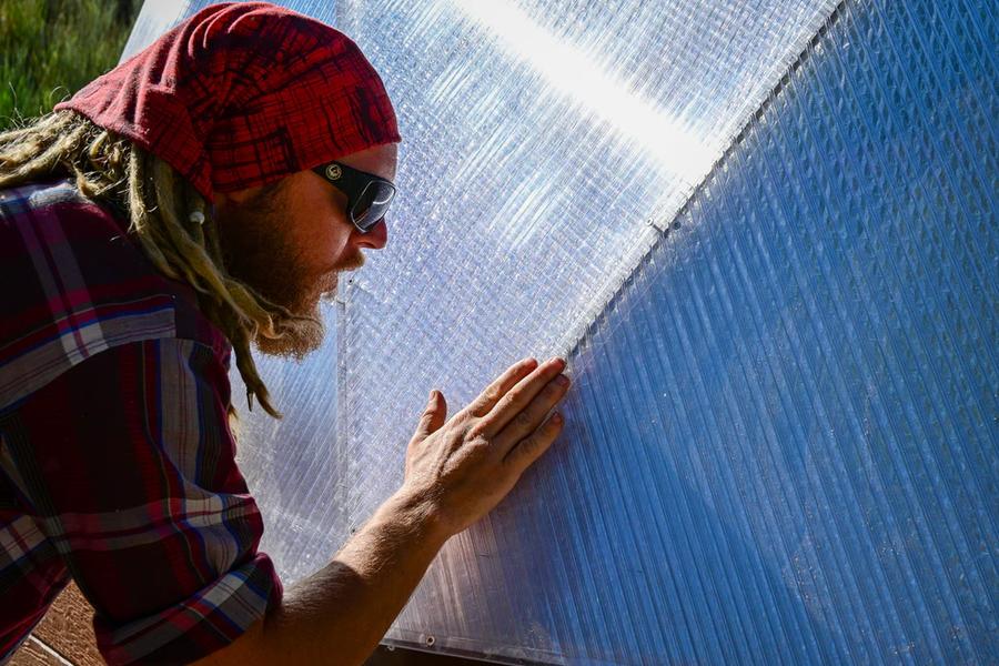 man running his hand along the outside seam of a geodesic greenhouse to apply pressure to the tape