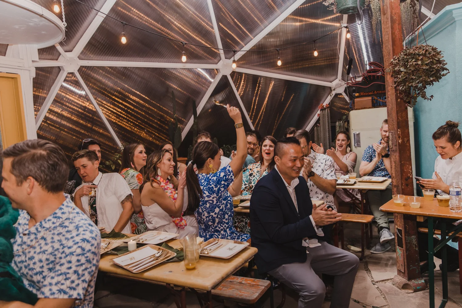 Large group of people seated and clapping inside a greenhouse bar