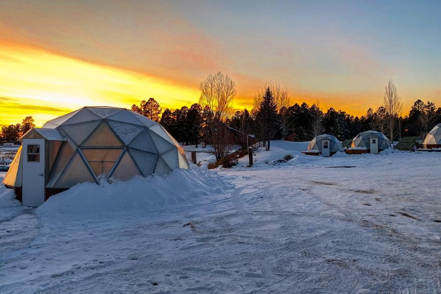 a geodesic greenhouse in the foreground with two in the background in a snowy landscape and sunset