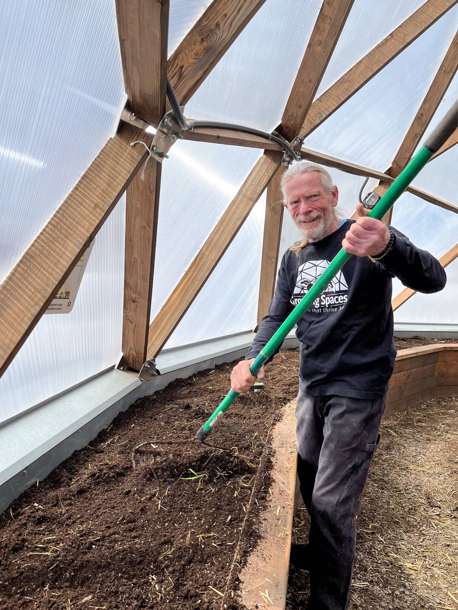 Man with a rake in a 42' Growing Dome preparing garden beds for planting
