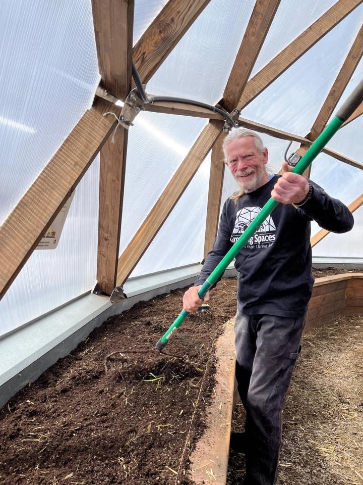Man with a rake in a 42' Growing Dome preparing garden beds for planting