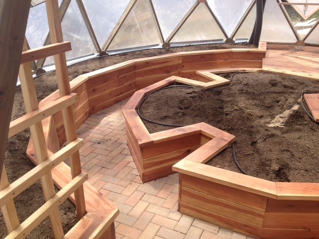 Redwood garden beds with irrigation system, soil, and brick pathway