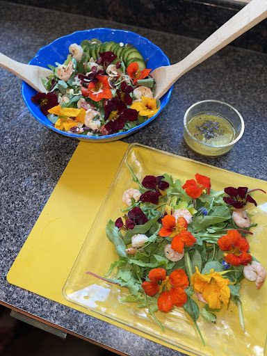 serving bowl of salad topped with nasturtiums on a countertop with dressing and beautiful plated salad