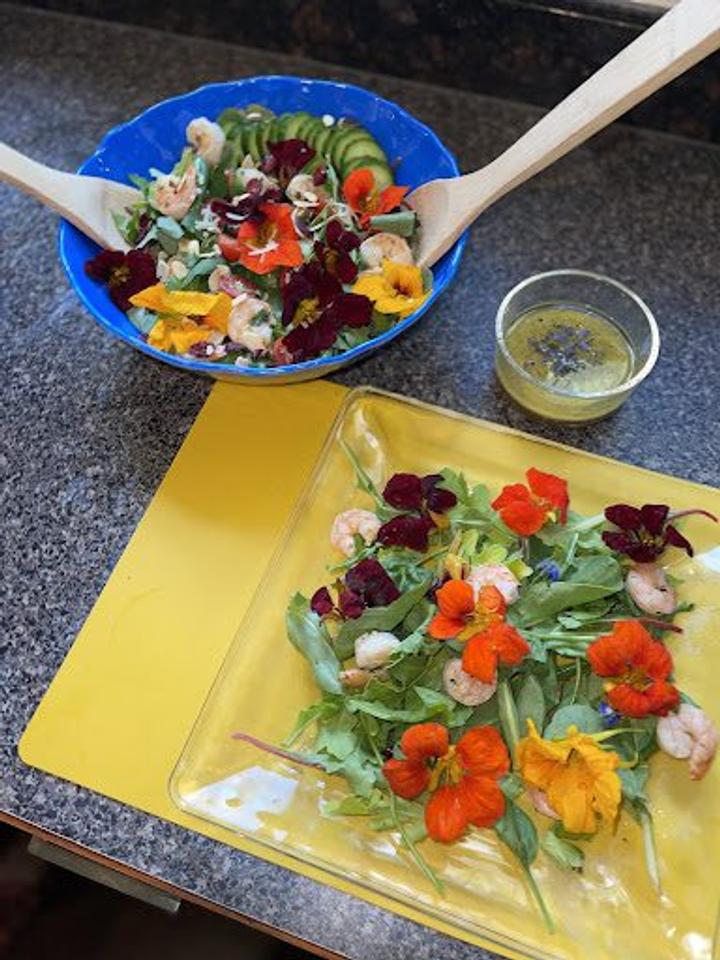serving bowl of salad topped with nasturtiums on a countertop with dressing and beautiful plated salad