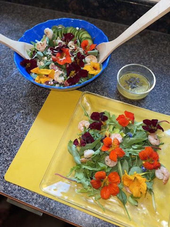 serving bowl of salad topped with nasturtiums on a countertop with dressing and beautiful plated salad