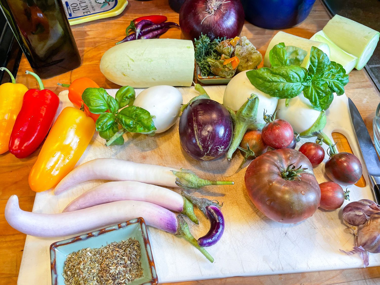 various raw ingredients on a cutting board ready to make ratatouille: fresh tomatoes, eggplant, herbs, peppers, and zucchini