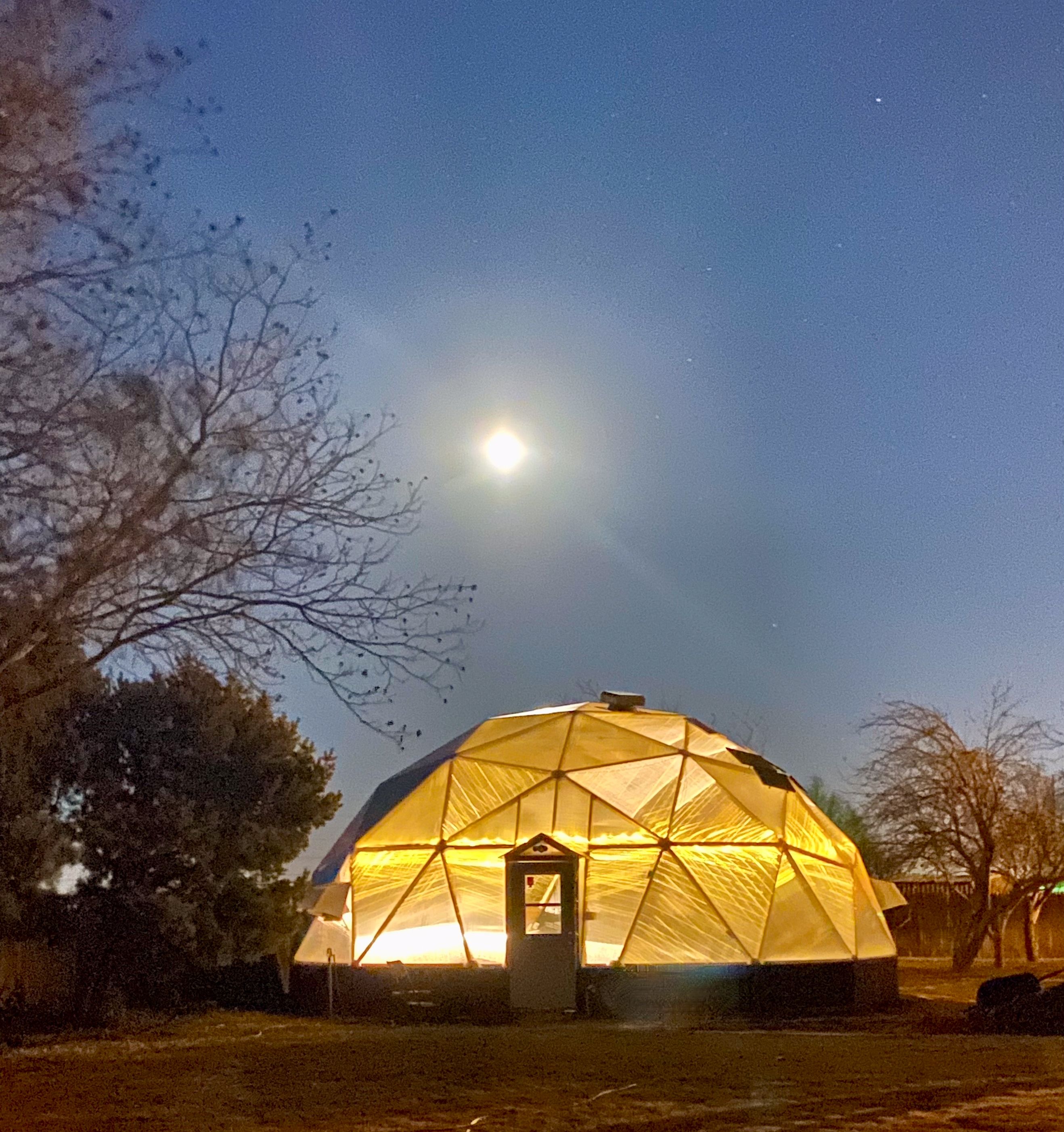 33 foot diameter growing dome illuminated from inside with warm yellow light underneath a full moon