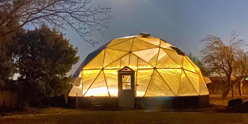 33 foot diameter growing dome illuminated from inside with warm yellow light underneath a full moon