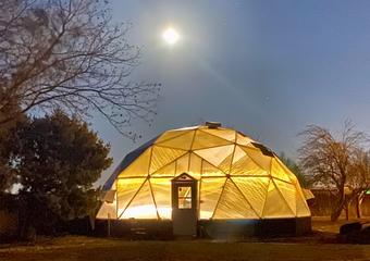 33 foot diameter growing dome illuminated from inside with warm yellow light underneath a full moon