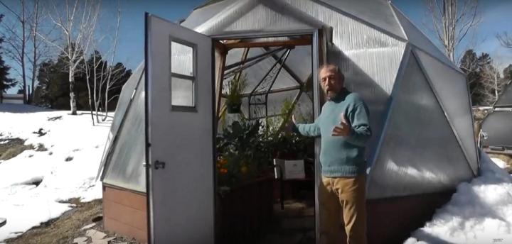 man showing green gardens during the winter inside a growing dome