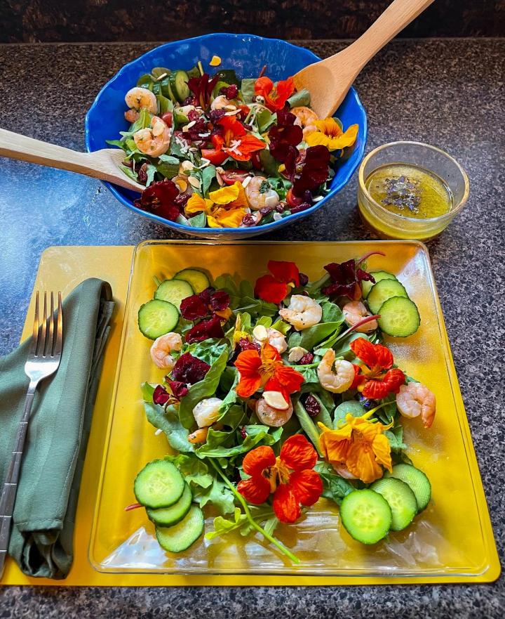 Shrimp and Nasturtium Salad with Pine Nuts salad bowl and dressing at the top of the photo with plate of salad ready to eat in the foreground