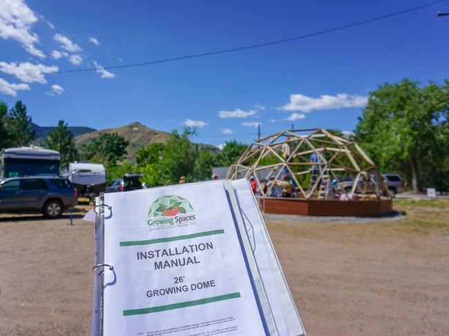 in the foreground an installation manual for a 26' Growing Dome greenhouse in the background the framework of the greenhouse has been installed