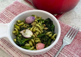 bowl of winter pesto pasta salad served up in front of the pot filled with pasta broccoli and radishes