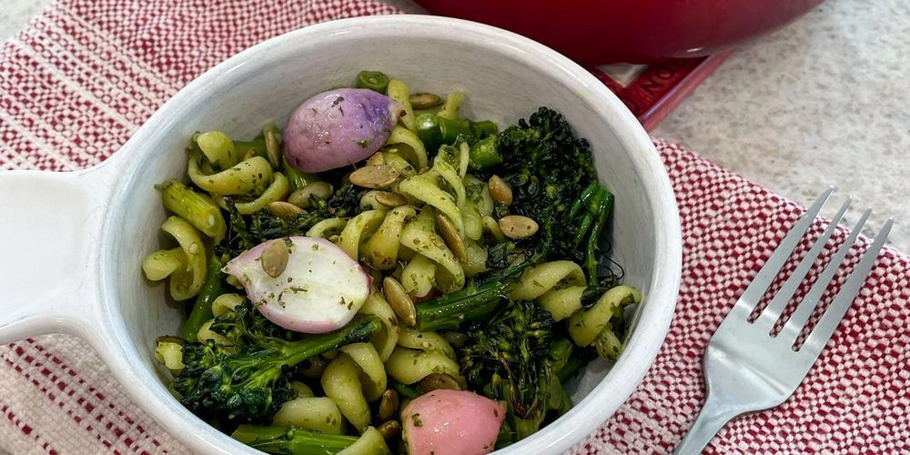bowl of winter pesto pasta salad served up in front of the pot filled with pasta broccoli and radishes