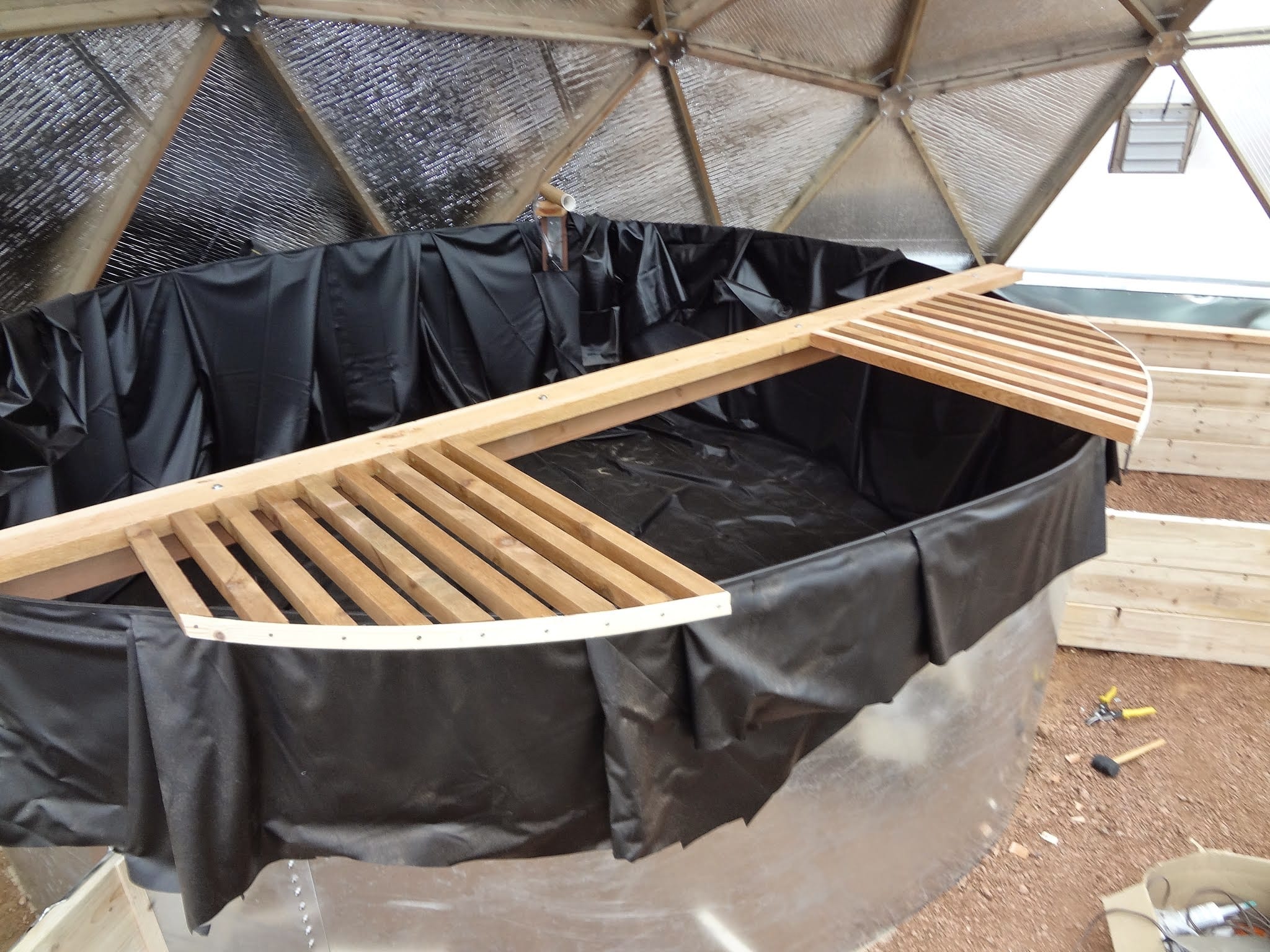wooden slat shelves across the above-ground pond in a geodesic greenhouse