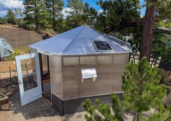 Exterior of a Growzebo backyard greenhouse with an open white front door and solar powered fan