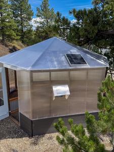 Exterior of a Growzebo backyard greenhouse with an open white front door and solar powered fan
