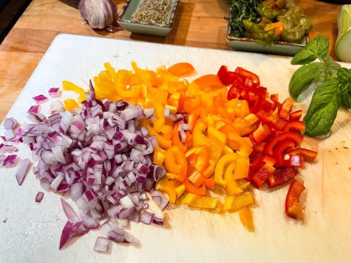 chopped red onions, and red, orange and yellow peppers, fresh basil and herbs on a cutting board