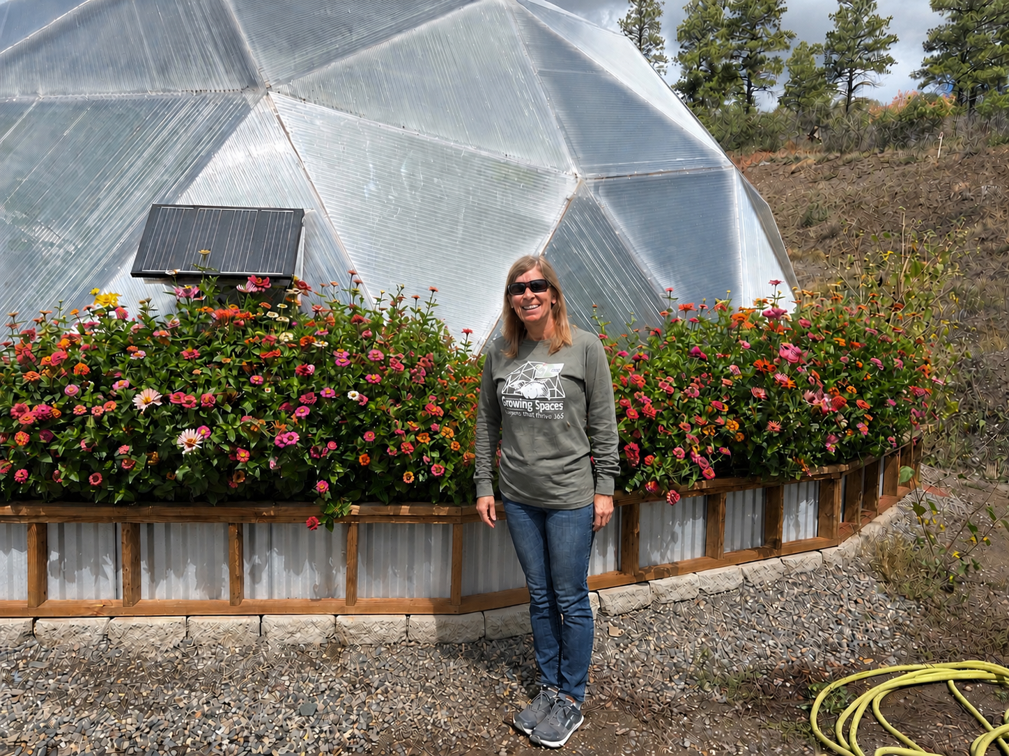 Woman standign outside a 33 foot diameter growing dome greenhouse surrounded by zinnia flowers