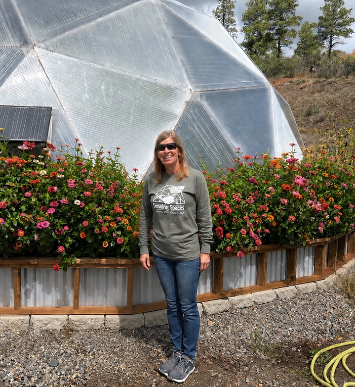 Woman standign outside a 33 foot diameter growing dome greenhouse surrounded by zinnia flowers