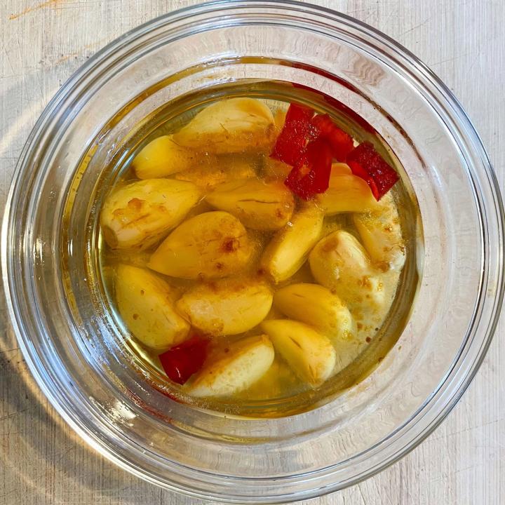 garlic roasted in oil with chiles in a clear glass bowl