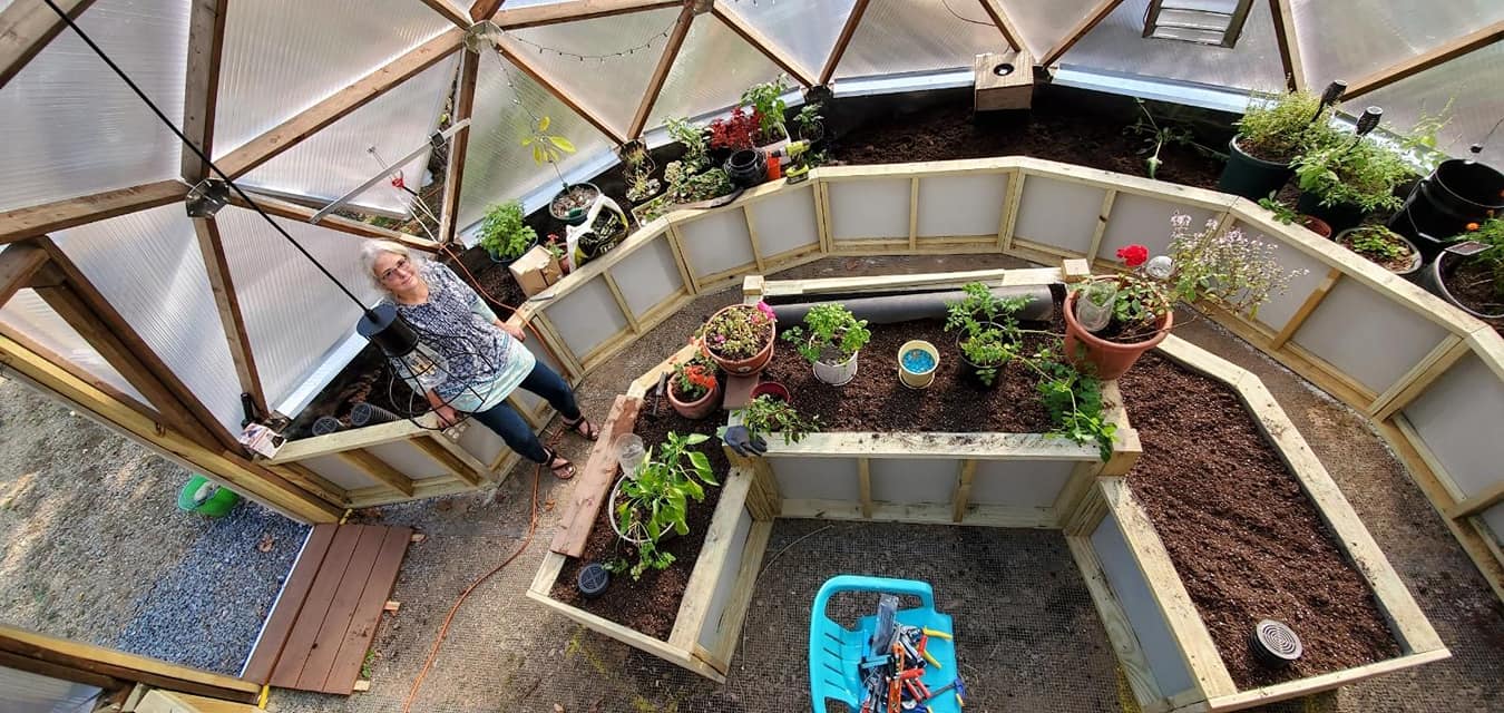 Grower standing inside a Growing Dome with curved beds and a central pond in New Hampshire