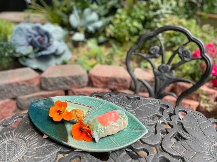 nasturtium spring roll on a green leaf-shaped plate, garnished with bright orange nasturtium flowers on a wrought iron table in a Growing Dome