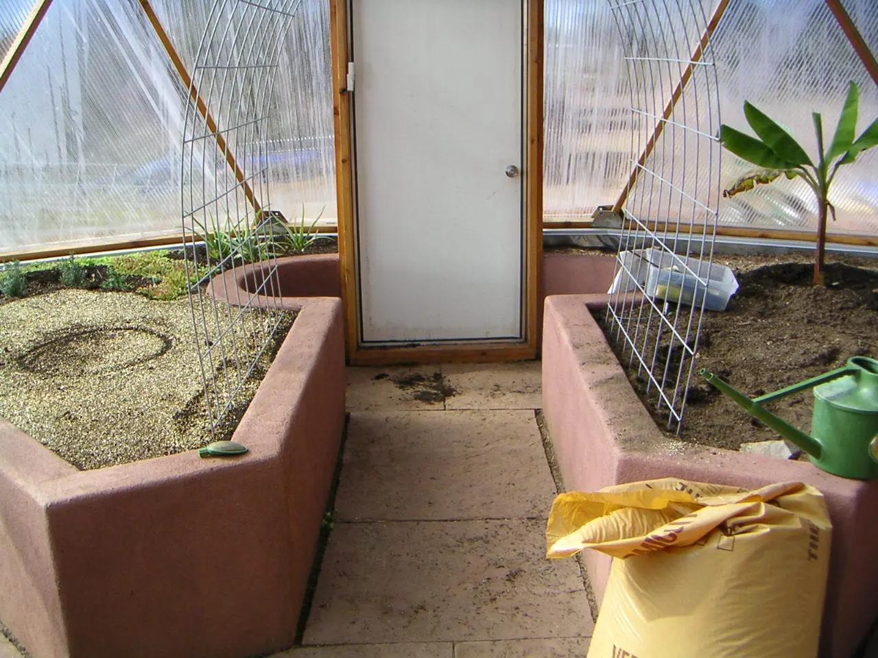 pink stucco finished raised beds around an entryway into the greenhouse