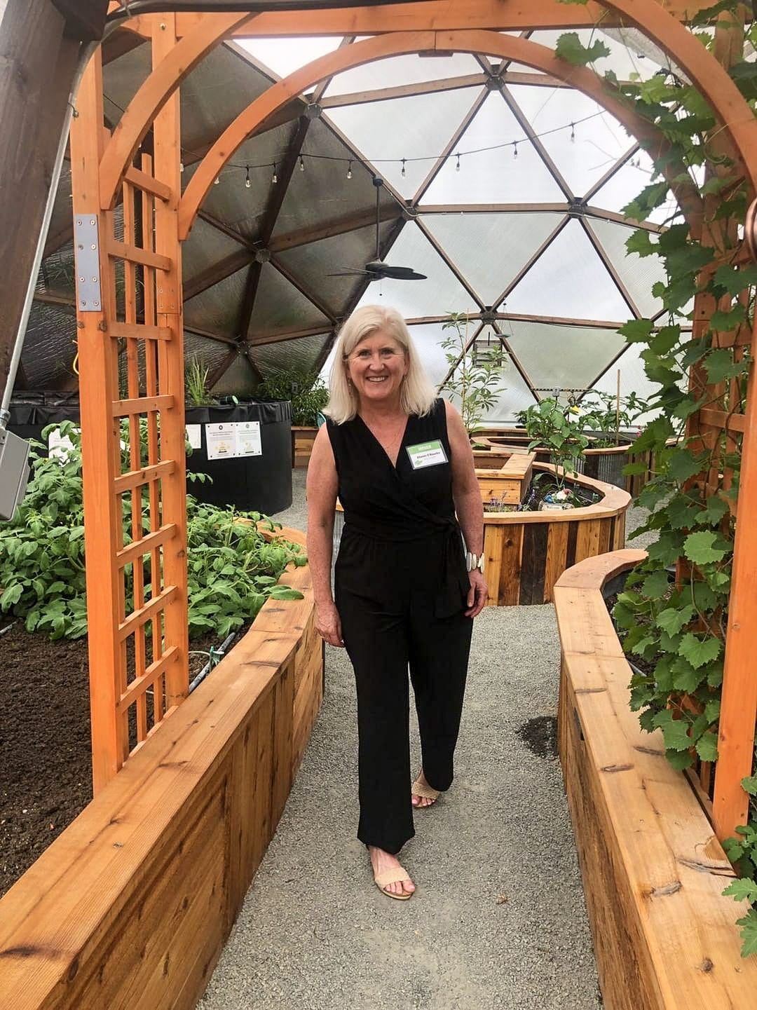 woman walking under a trellis supporting grape vines inside of a growing dome greenhouse