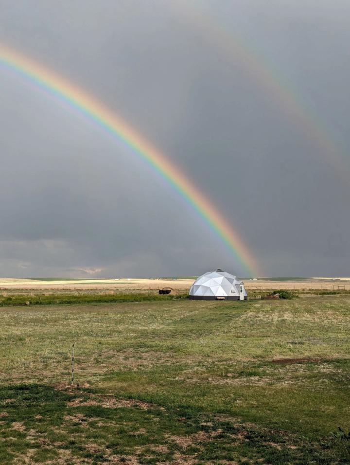 Field with dark clouds overhead and double rainbow shining over the dome.