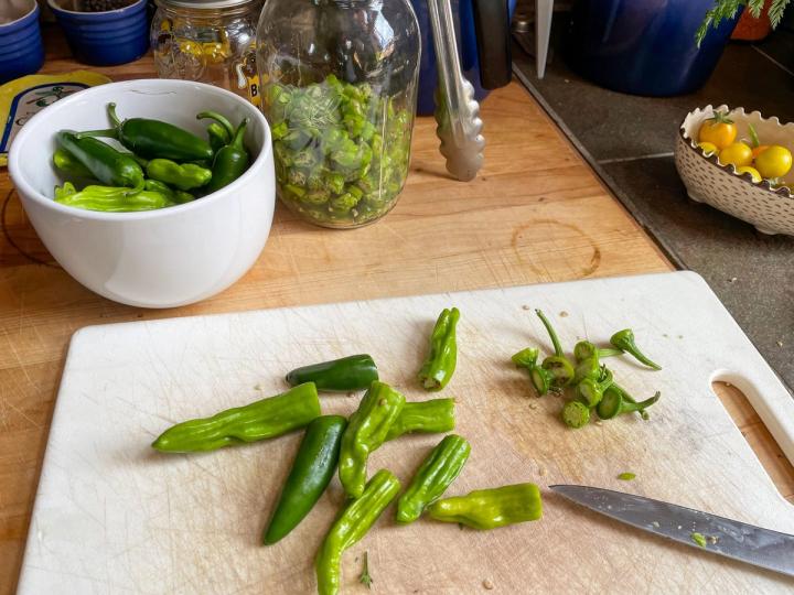 slicing peppers on a cutting board, bowl full of whole peppers and quart jar full of sliced peppers in the background