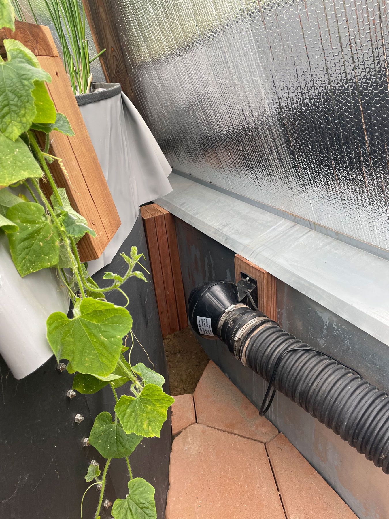 electric undersoil fan attached to the greenhouse wall behind the above-ground pond