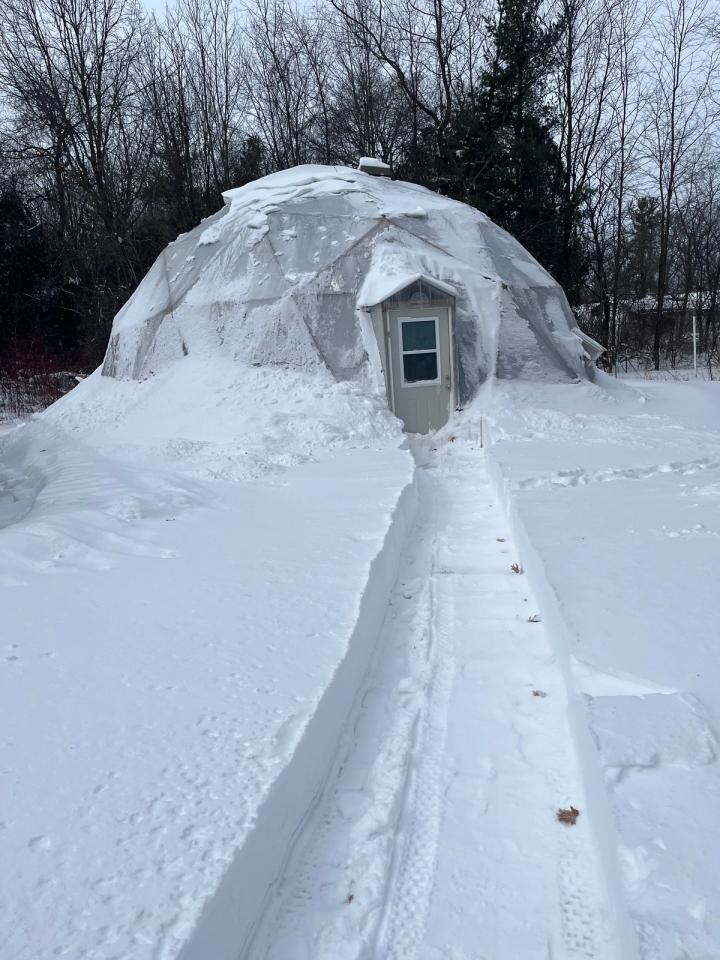 A Growing Dome greenhouse covered in snow with a path shoveled to the greenhouse
