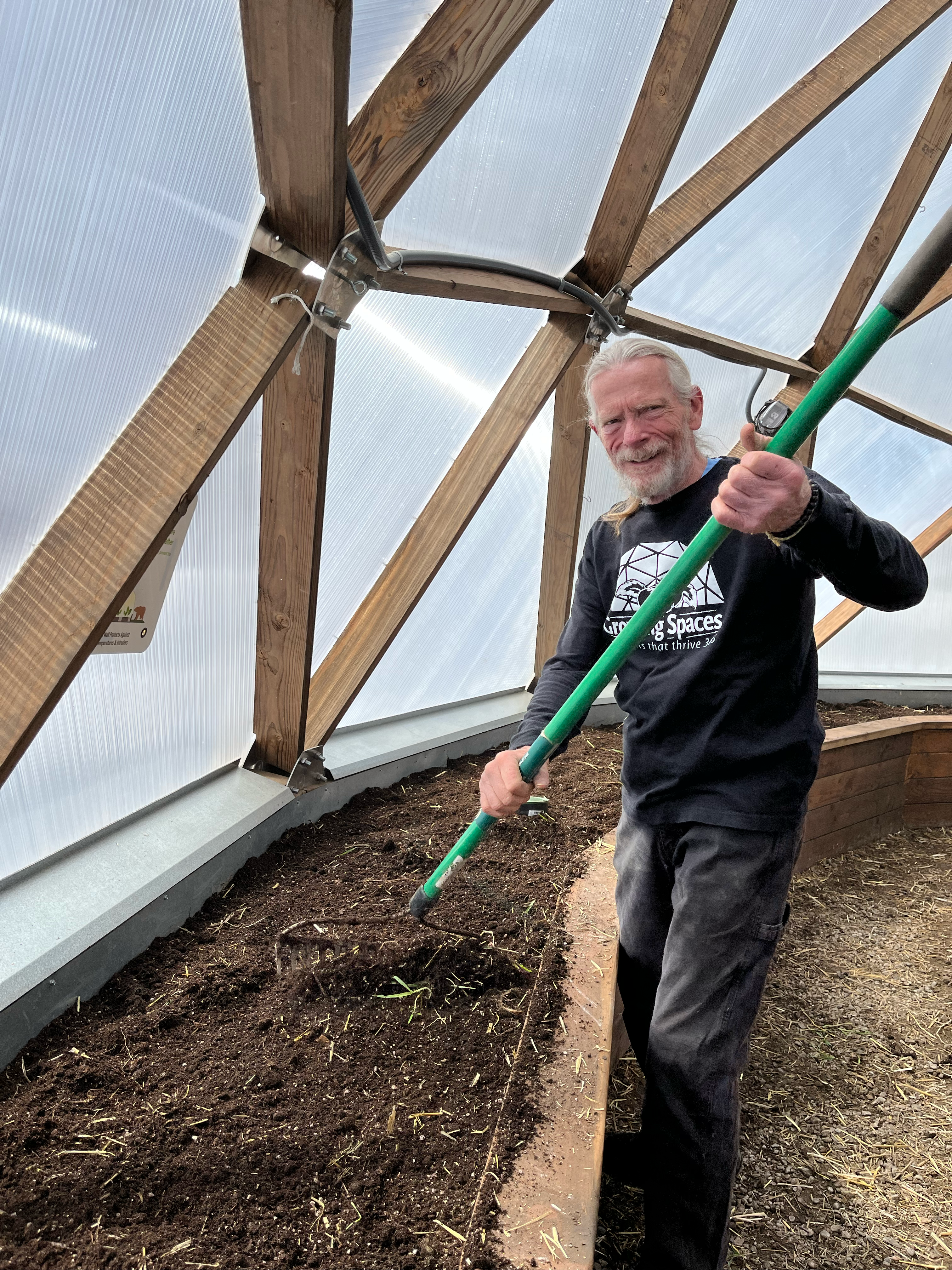 A man raking a fresh layer of topsoil to level a raised garden bed