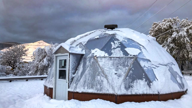 Growing Dome greenhouse covered in a light dusting of snow with a dark and stormy sky behind