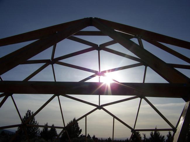 the sun silhouetting the struts of a geodesic dome greenhouse being constructed