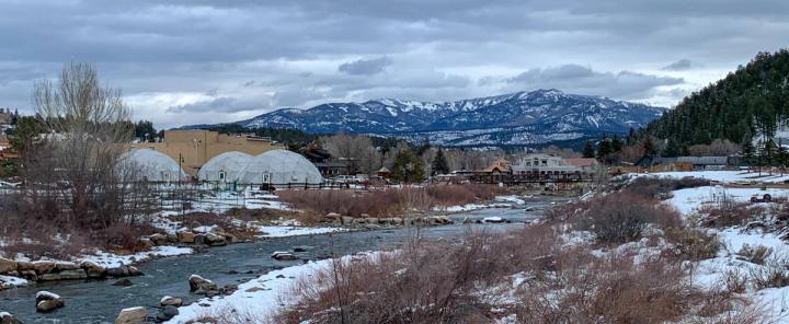 Three 42' Growing Dome Greenhouses positioned next to the San Juan River with the Springs Resort bathhouse and snow-capped San Juan Mountains in the distance