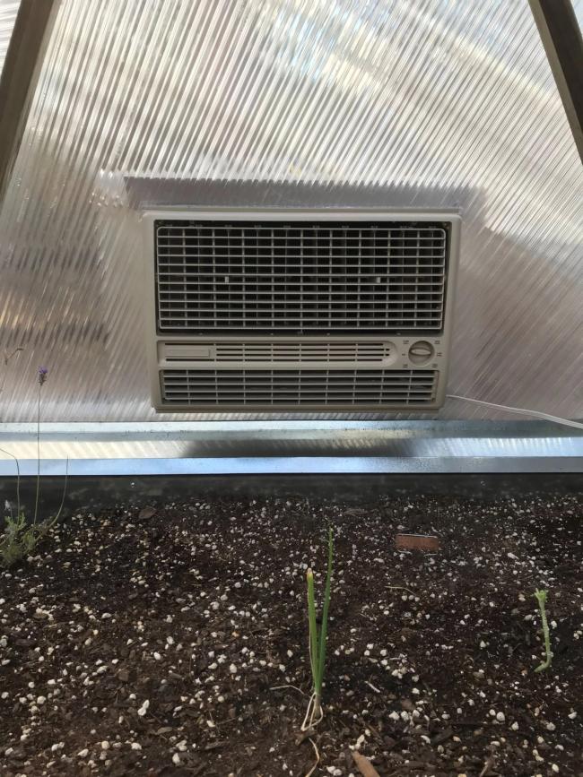 A window mount AC unit mounted in a polycarbonate panel in a greenhouse