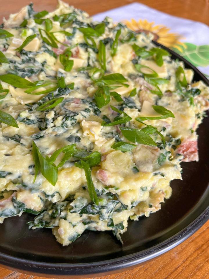 Colcannon plated on a black plate with green onions sprinkled on top