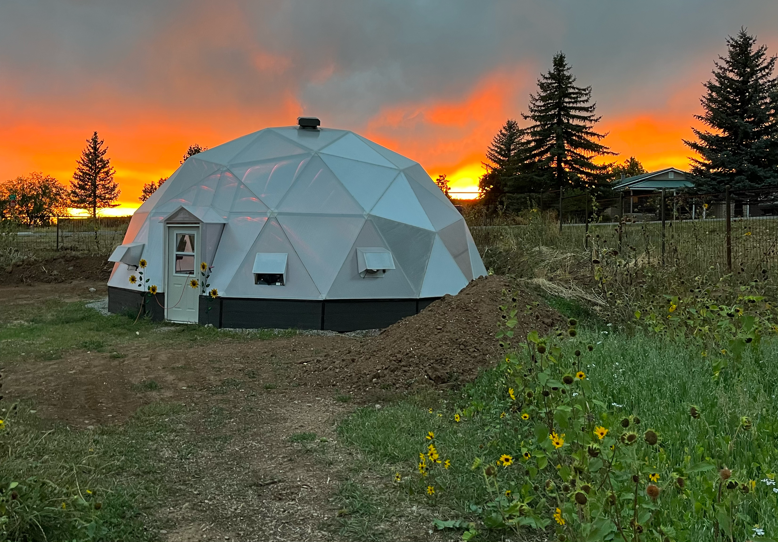 33 foot growing dome greenhouse with a vibrant orange sunset and small sunflowers