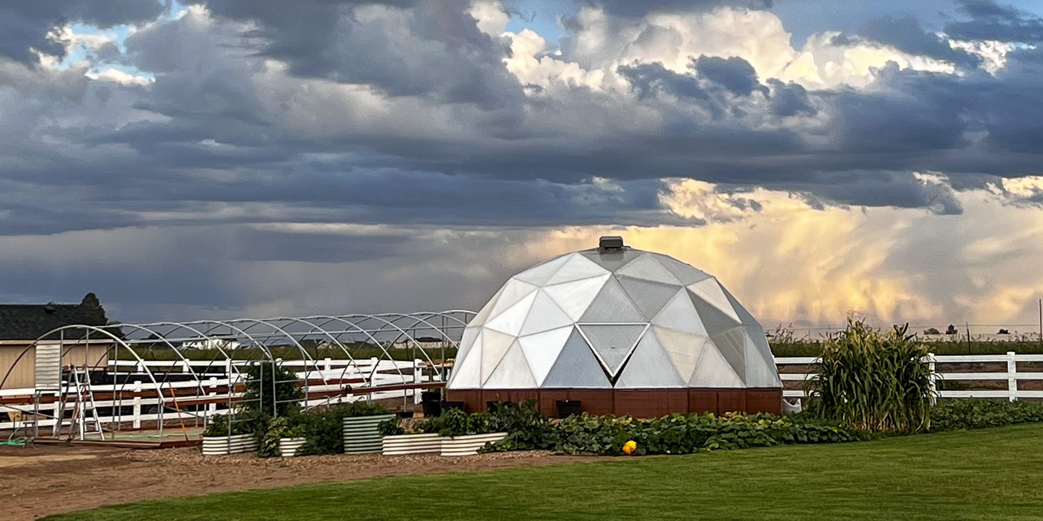 Growing Dome greenhouse with outdoor garden surrounding it and a hoop house frame to the left
