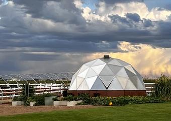 Growing Dome greenhouse with outdoor garden surrounding it and a hoop house frame to the left