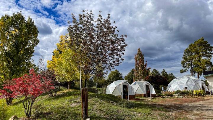 A 15', 18' and 26' Growing Dome greenhouse in a row with fall foliage surrounding and an ominous sky