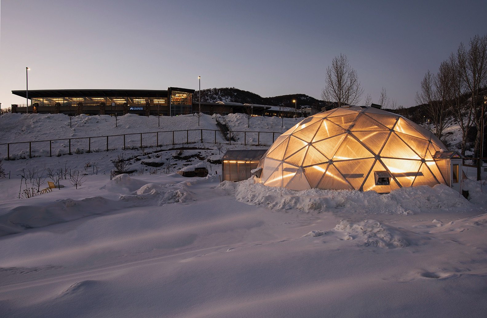 Growing Dome greenhouse illuminated at dusk in a snow-covered landscape